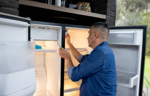 Latin American handyman fixing a fridge at a house - domestic life concepts